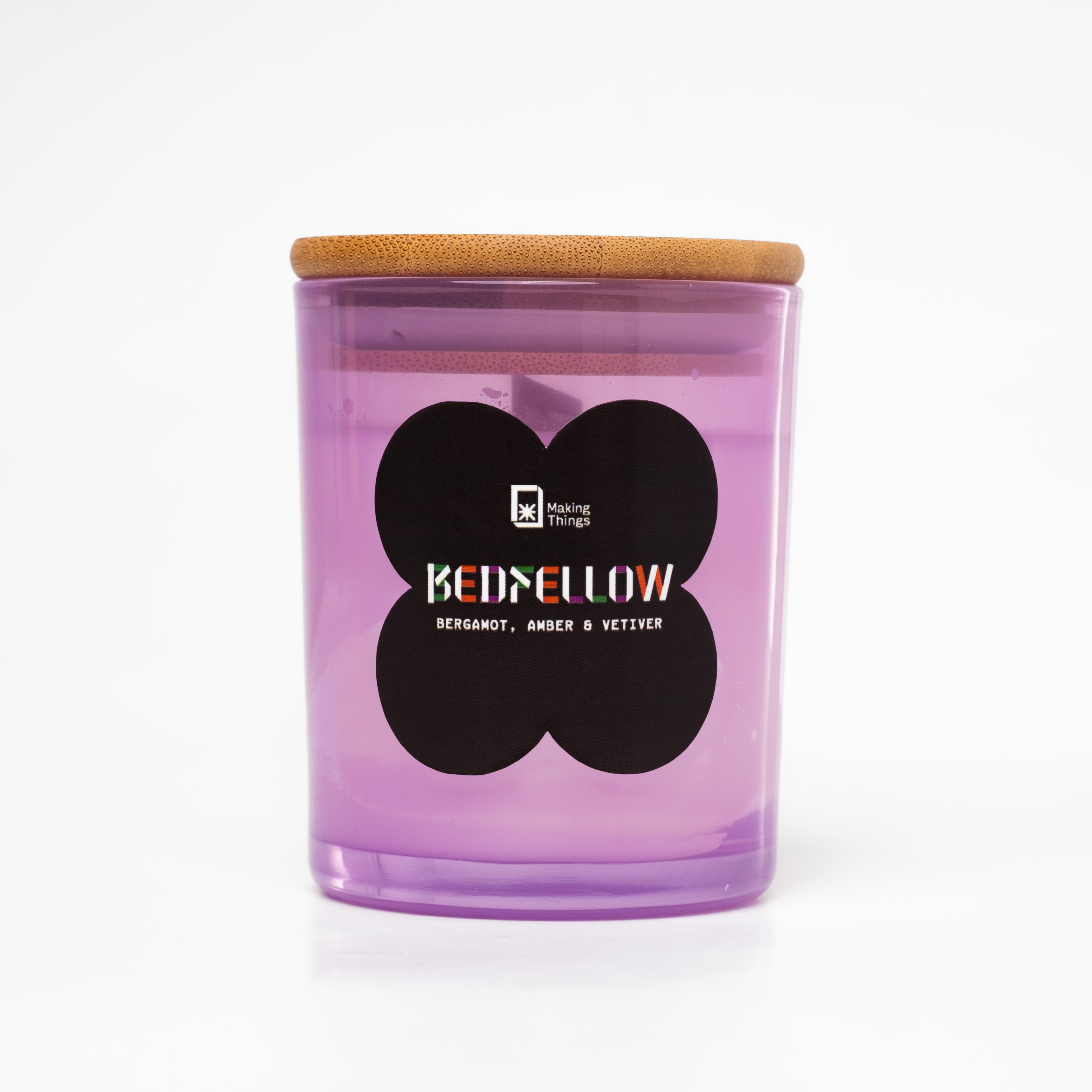 A scented candle with notes of bergamot, amber, and vetiver. It is packaged in a purple jar with a wooden lid.