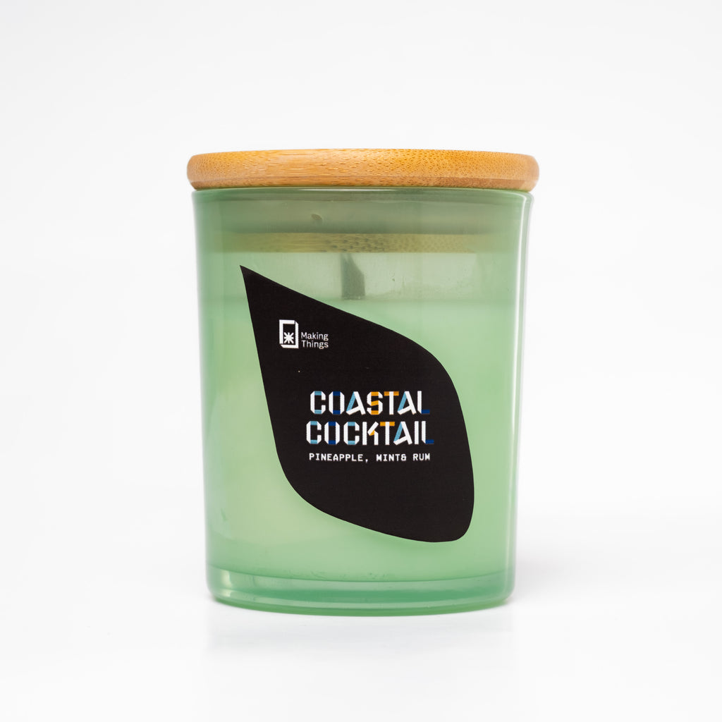 A scented candle with notes of pineapple, mint, and rum. It is packaged in a green jar with a wooden lid.