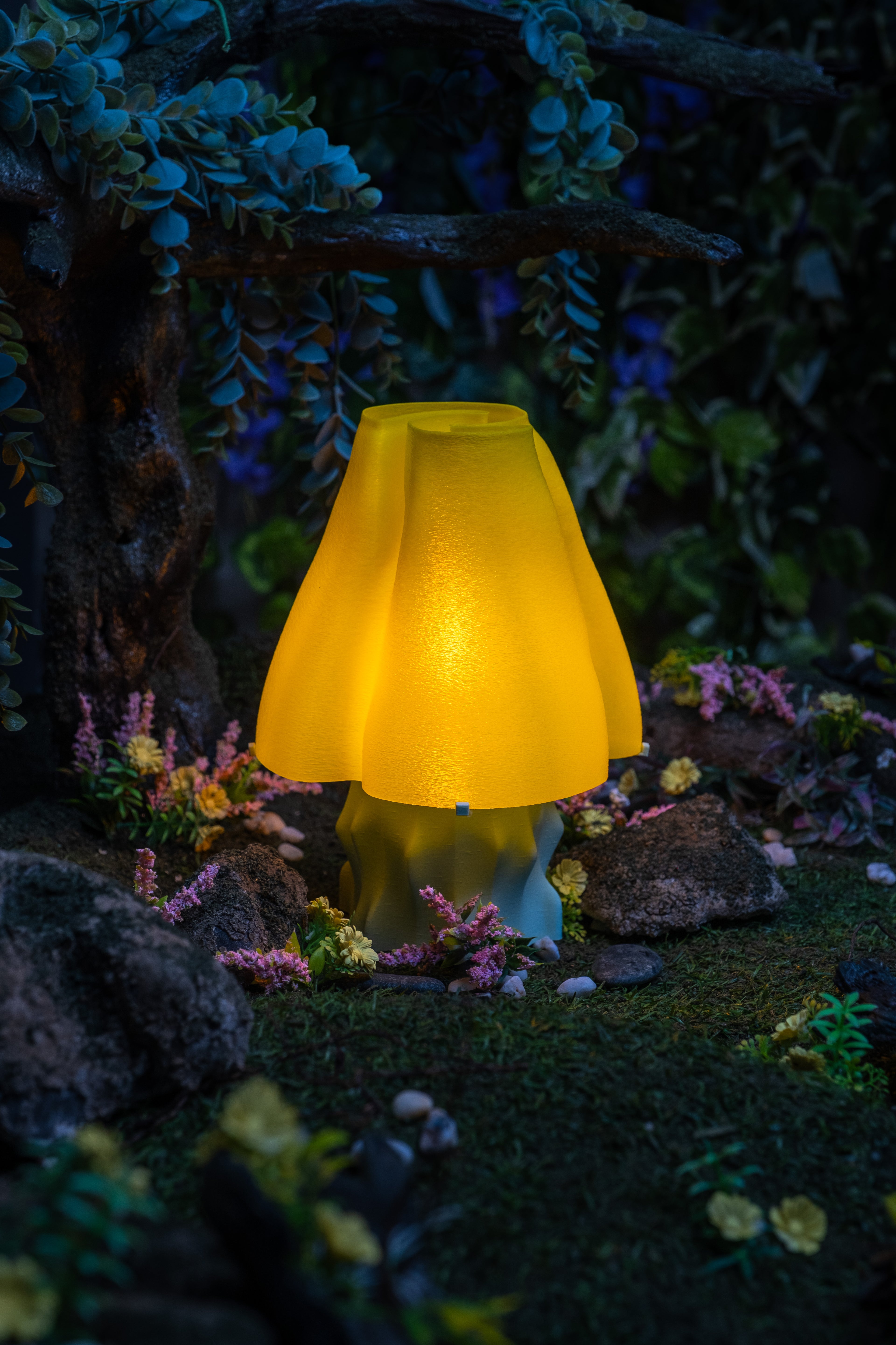 A yellow, mushroom-shaped, 3D-printed lamp alight on a lush forest floor.