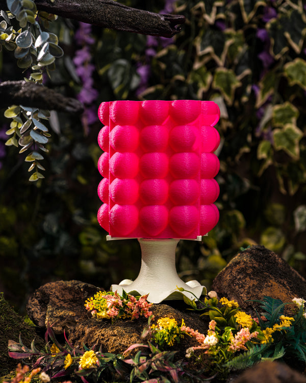 A pink, bubble-textured 3D-printed lamp on a lush forest floor.