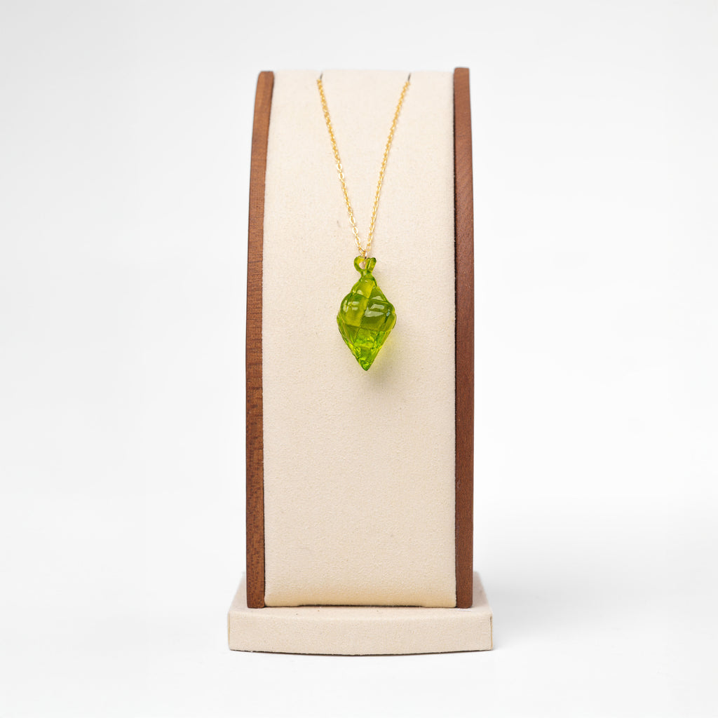 A necklace with a resin-printed, green, puso pendant with a gold non-tarnish chain. The necklace is displayed on a stand.