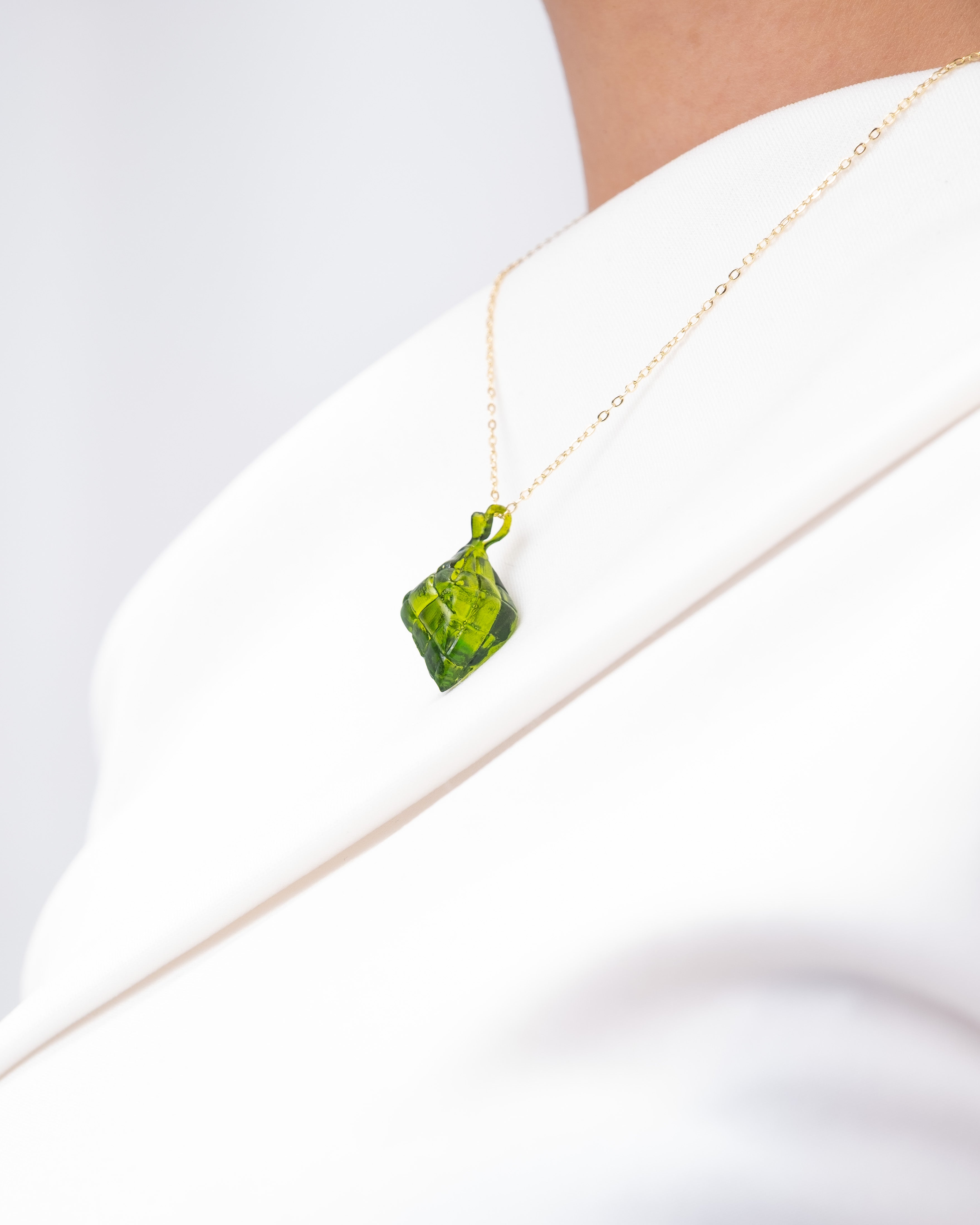 A necklace with a resin-printed, green, puso pendant with a gold non-tarnish chain. The necklace is worn.