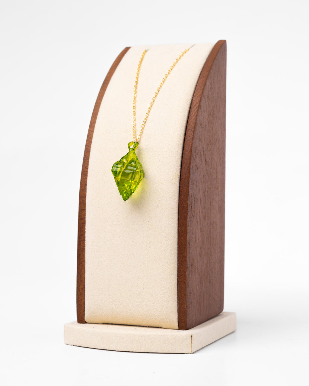 A necklace with a resin-printed, green, puso pendant with a gold non-tarnish chain. The necklace is displayed on a stand.