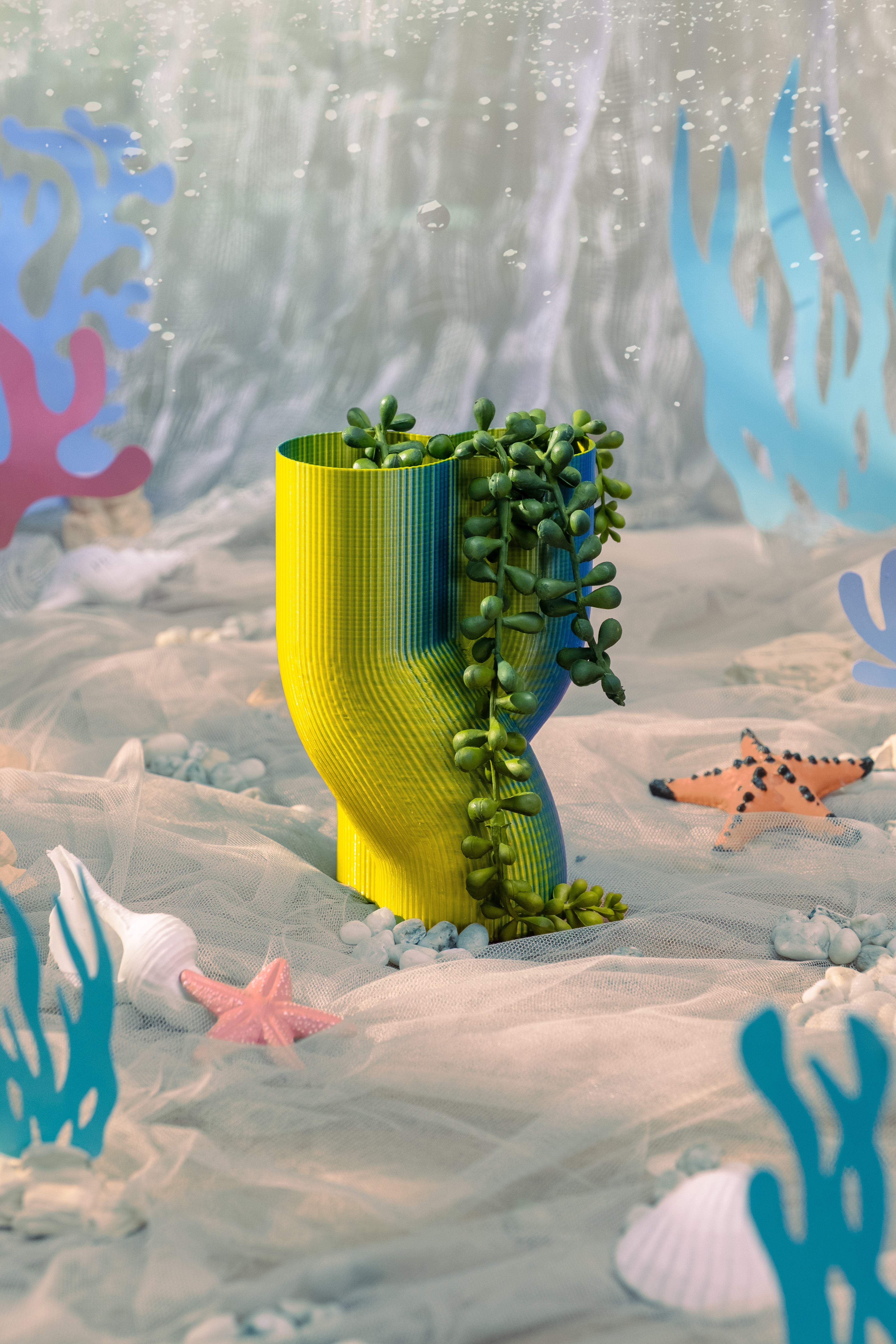 A 3D-printed iridescent vase with a hanging plant inside.