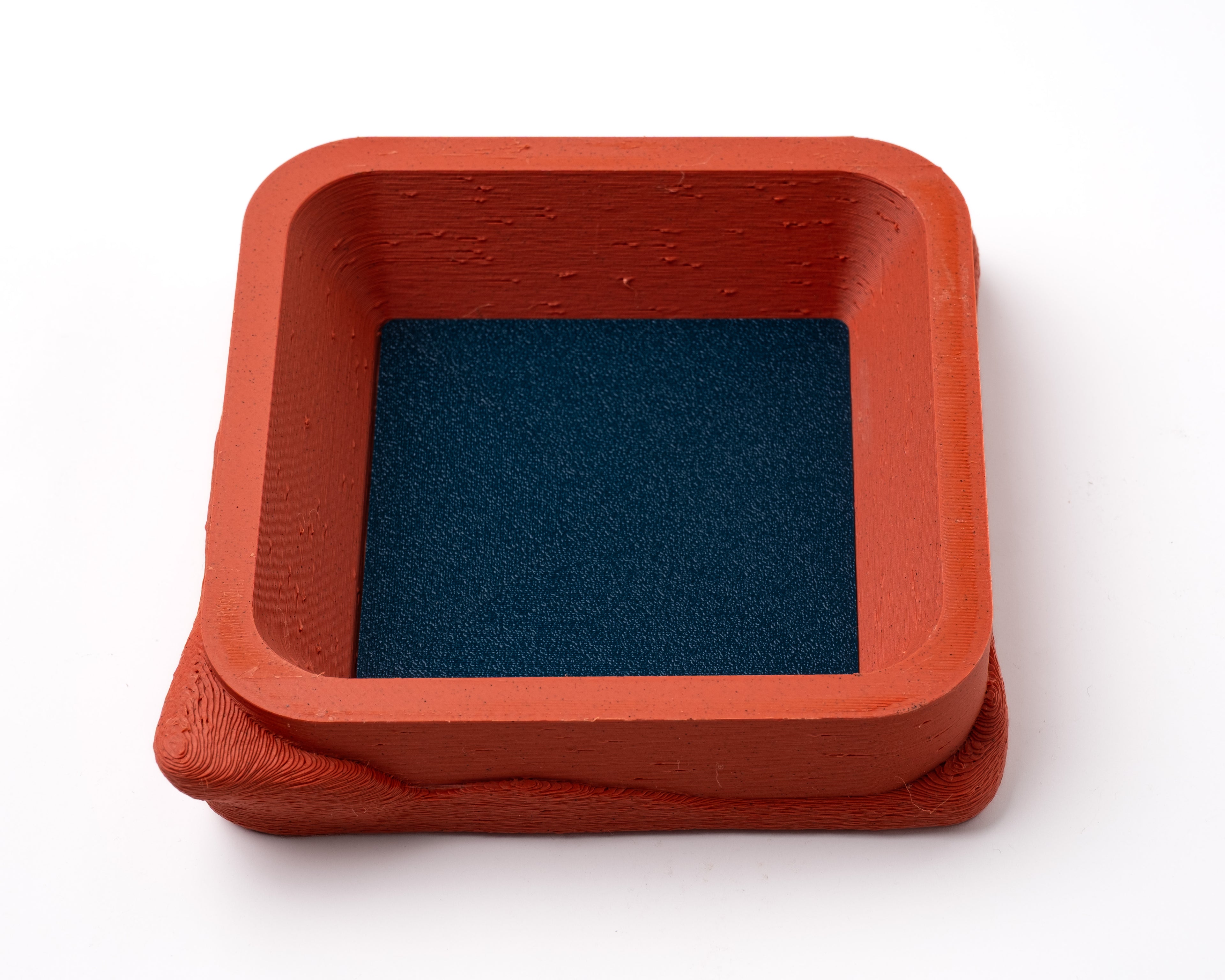 A decorative, square, orange catch all with an interchangeable coaster. The coaster inside is in black. 