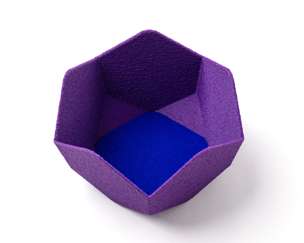 A decorative, geometric, violet catch all with an interchangeable coaster. The coaster inside is in blue.