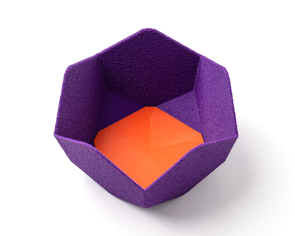 A decorative, geometric, violet catch all with an interchangeable coaster. The coaster inside is in orange. 