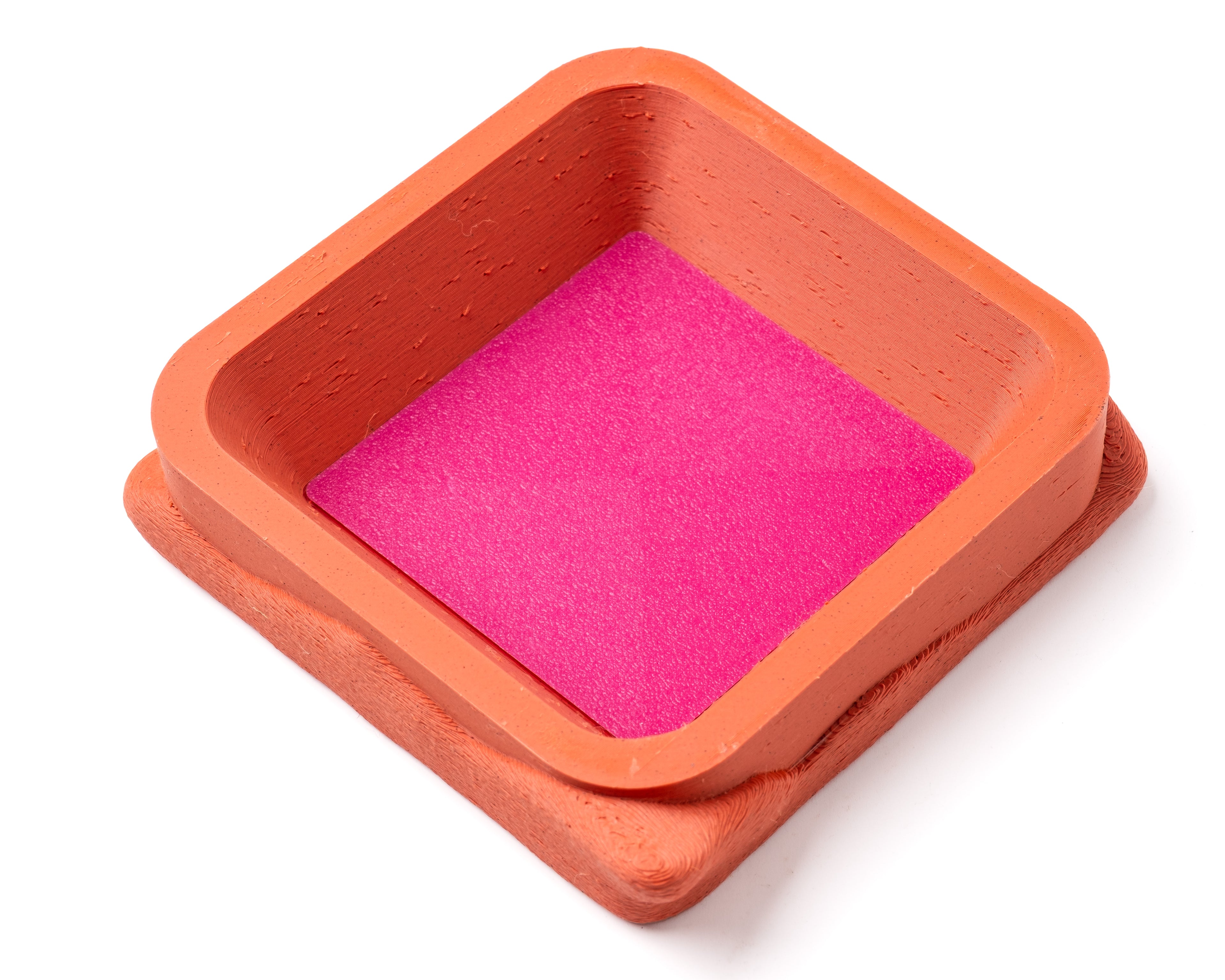 A decorative, square, orange catch all with an interchangeable coaster. The coaster inside is in hot pink. 