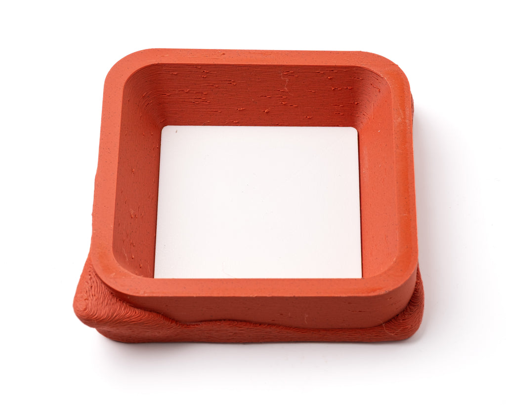 A decorative, square, orange catch all with an interchangeable coaster. The coaster inside is in white. 