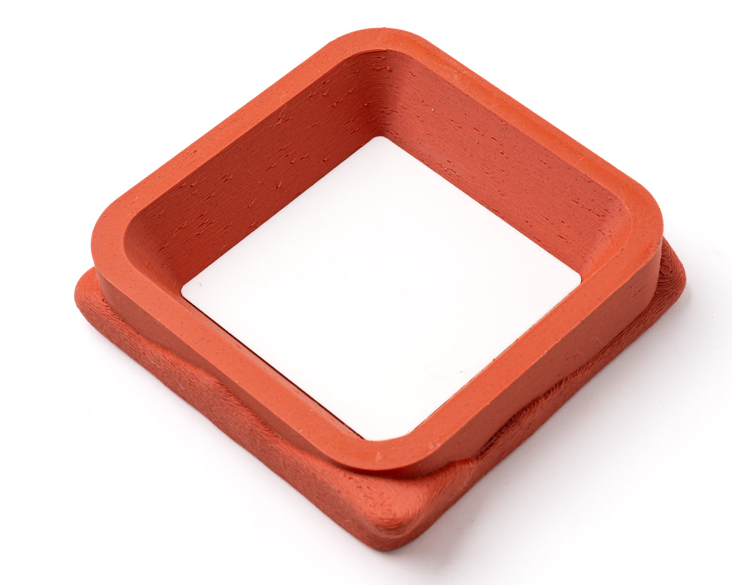 A decorative, square, orange catch all with an interchangeable coaster. The coaster inside is in white.