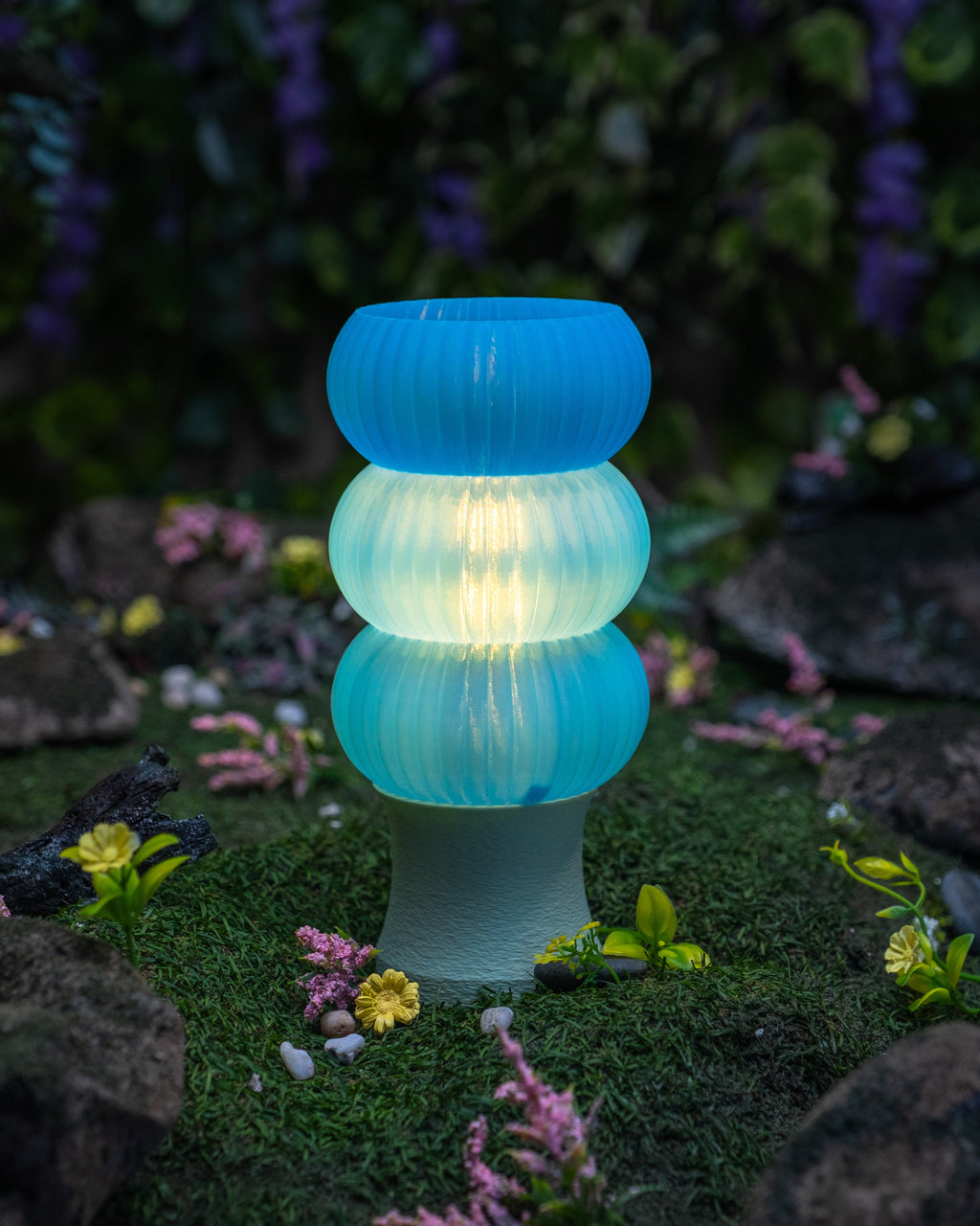 A blue 3D-printed lamp alight on a lush forest floor.