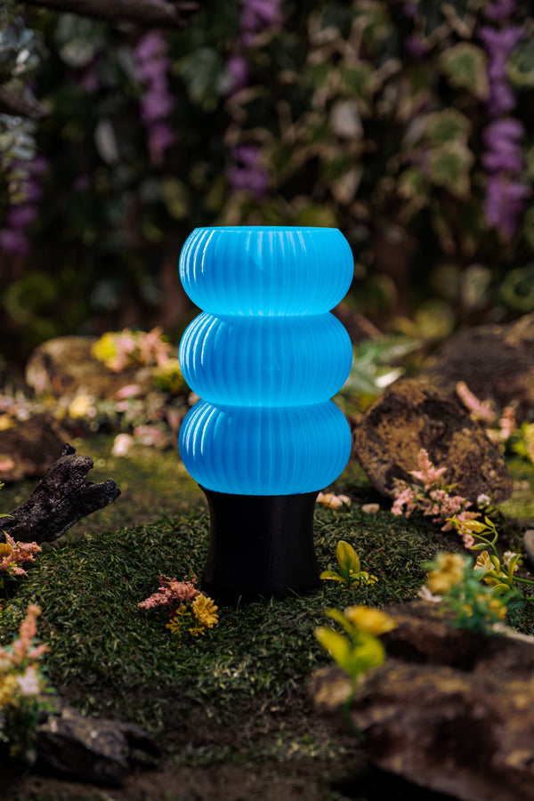A blue 3D-printed lamp on a lush forest floor.