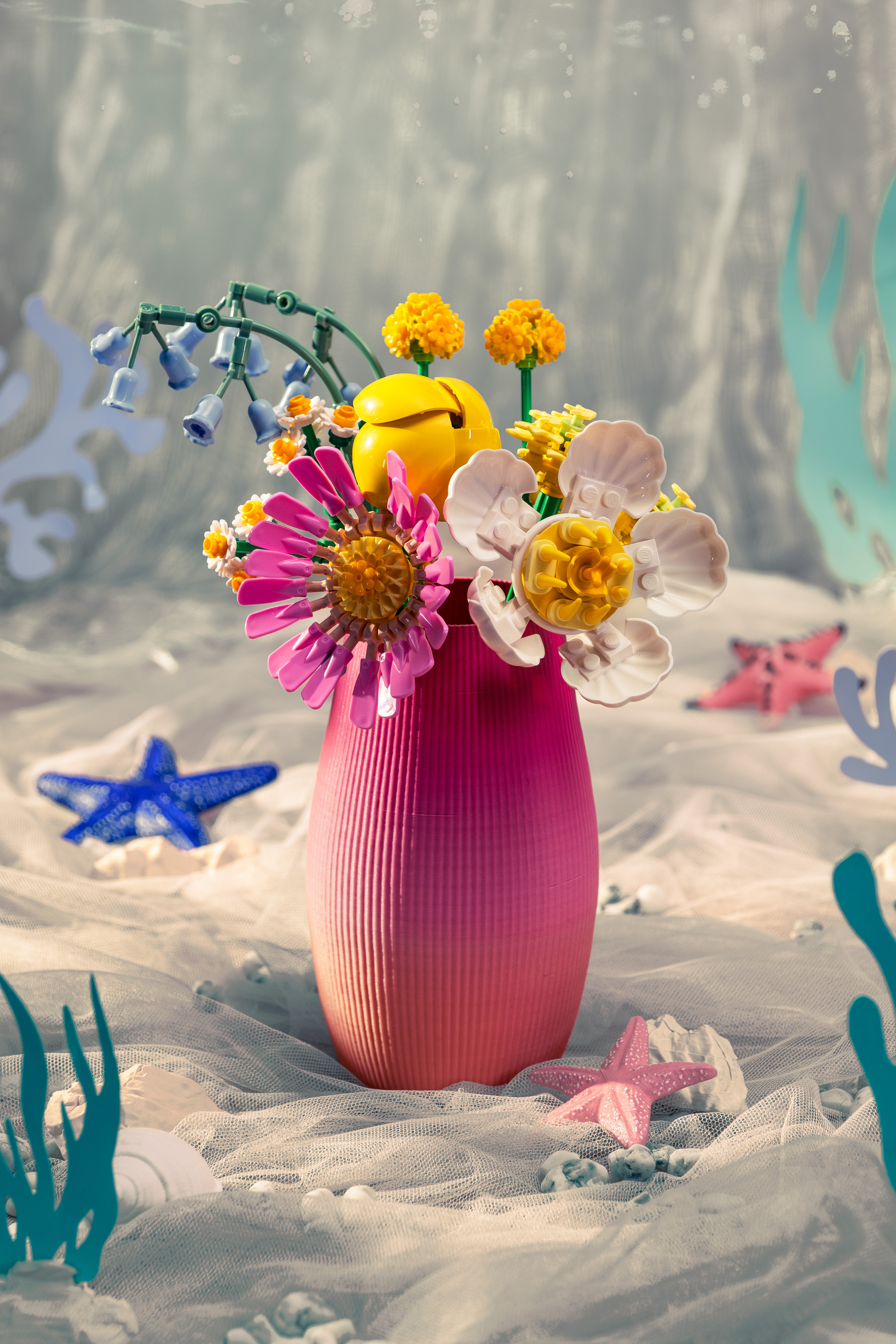 A 3D-printed vase that uses a multi-colored filament that creates a pink to light orange gradient. There are brick flowers inside the vase.