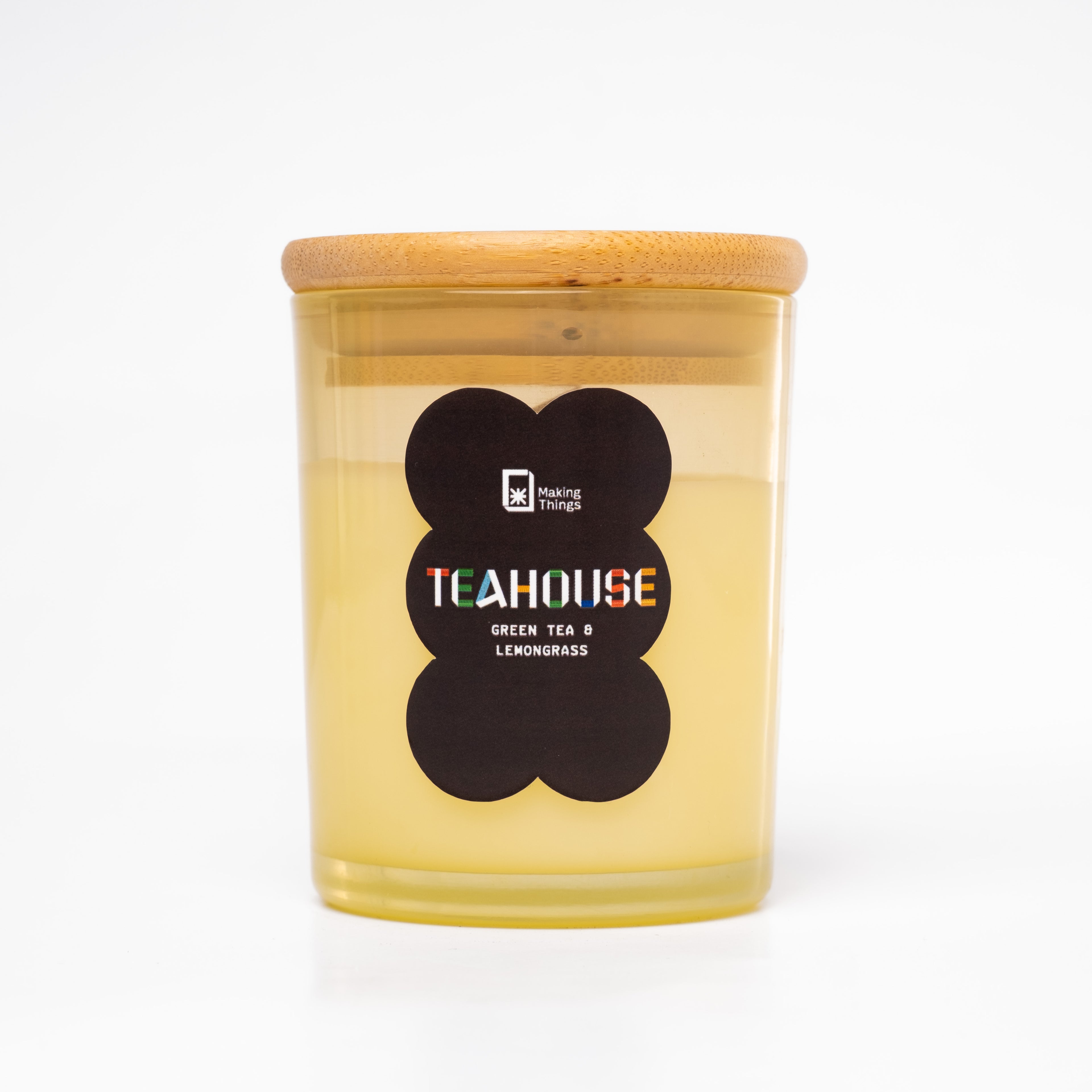 A scented candle with notes of green tea and lemongrass. It is packaged in a yellow jar with a wooden lid.