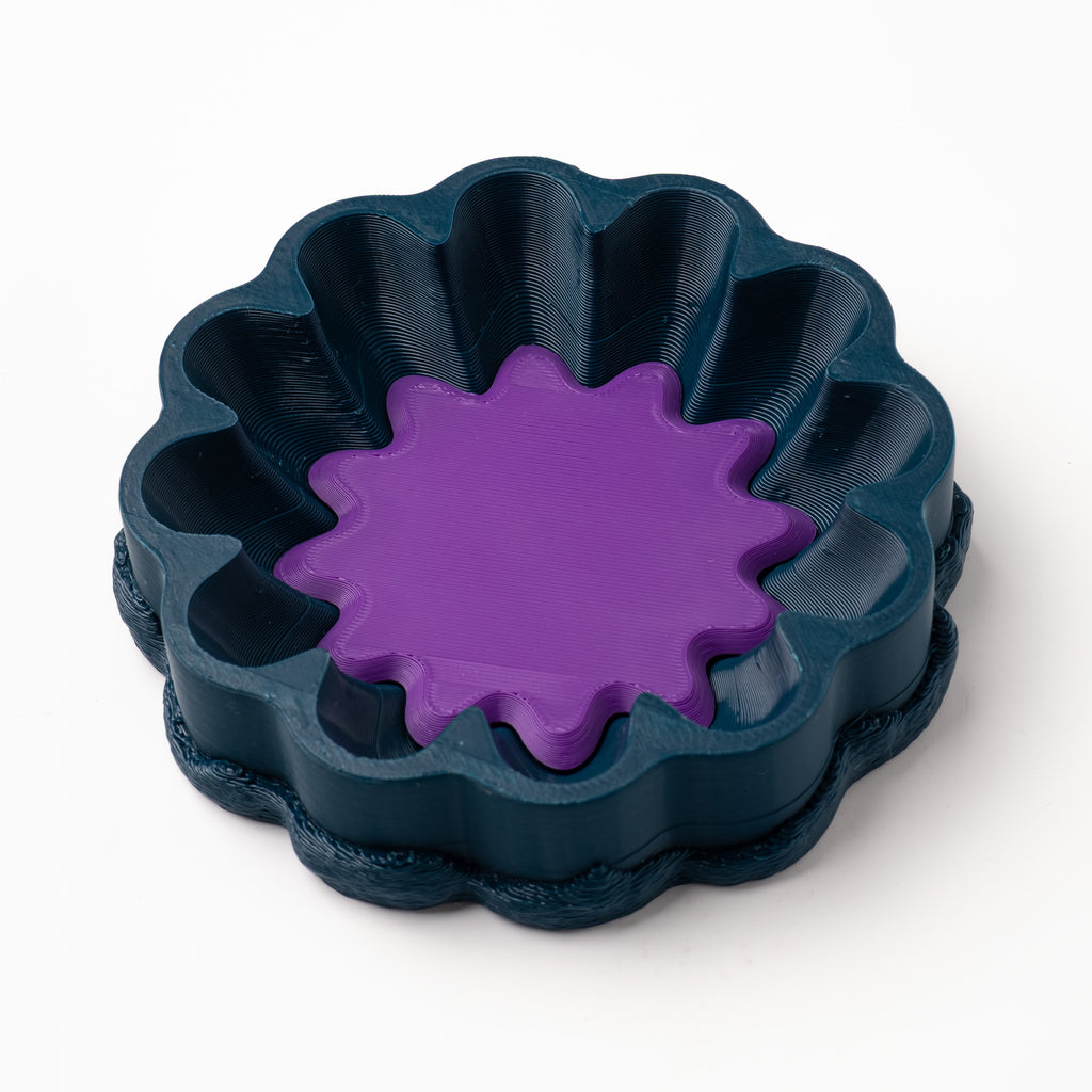 A decorative, floral-shaped, blue-green catch all with an interchangeable coaster. The coaster inside is in orange. 