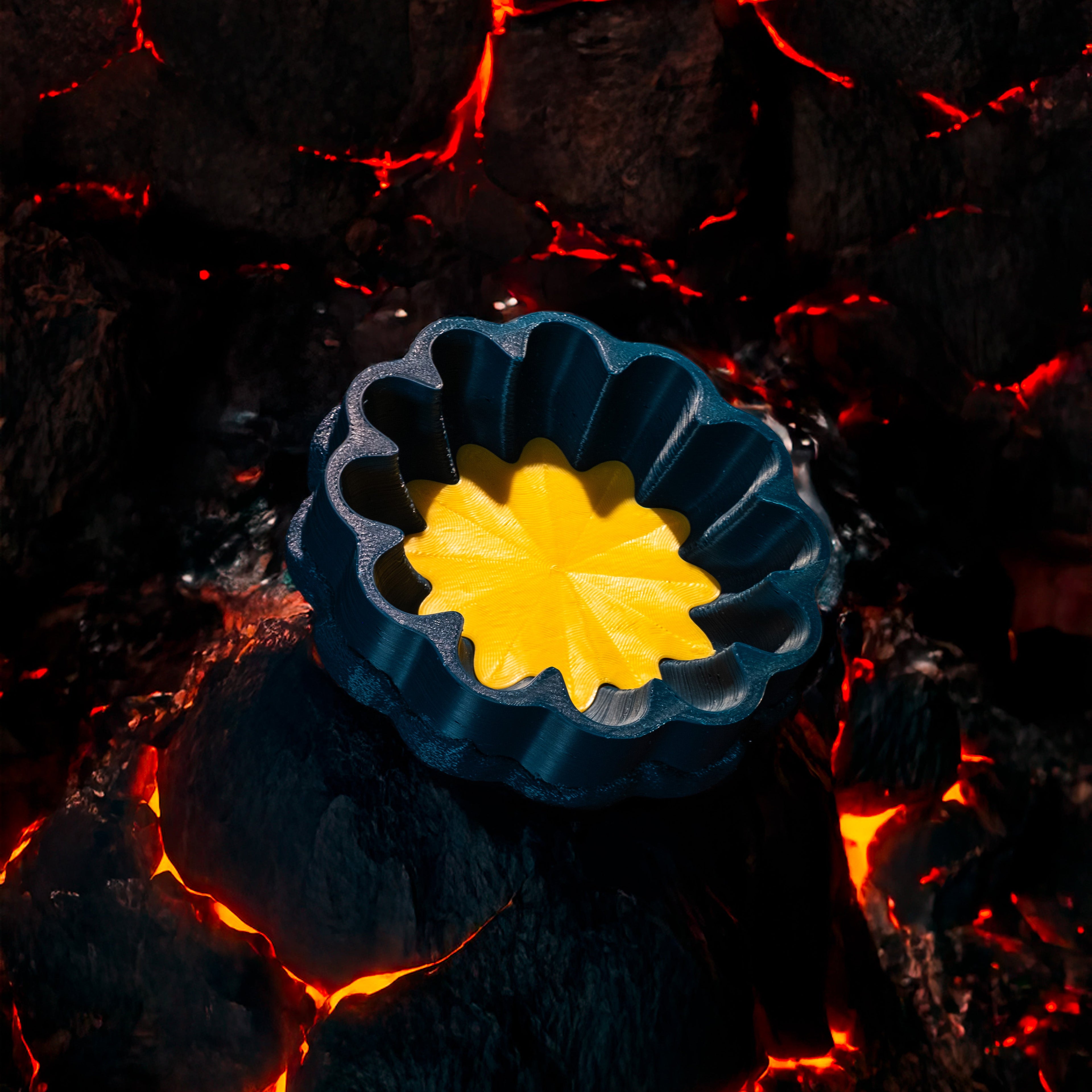 A decorative, floral-shaped, blue-green catch all with an interchangeable coaster. The coaster inside is in yellow. The catchall is against rocks cooling from streams of lava.