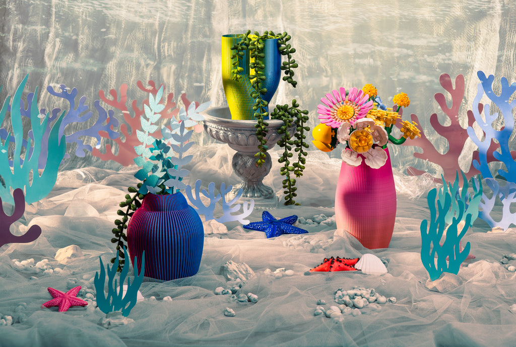 A group photo of 3D-printed vases. From left to right, there's a blue and purple iridescent vase, a green and blue iridescent vase, and a pink to orange vase.